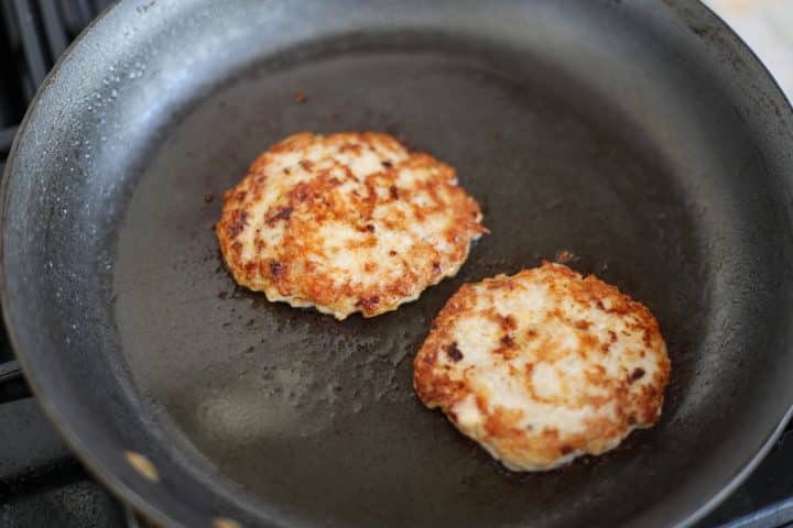 two burgers cooking in a hot skillet.