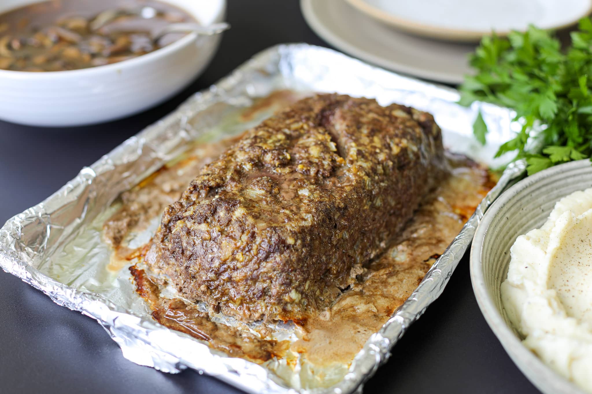 fresh out of the oven baked meatloaf with mushroom gravy on a sheet of aluminum foil.