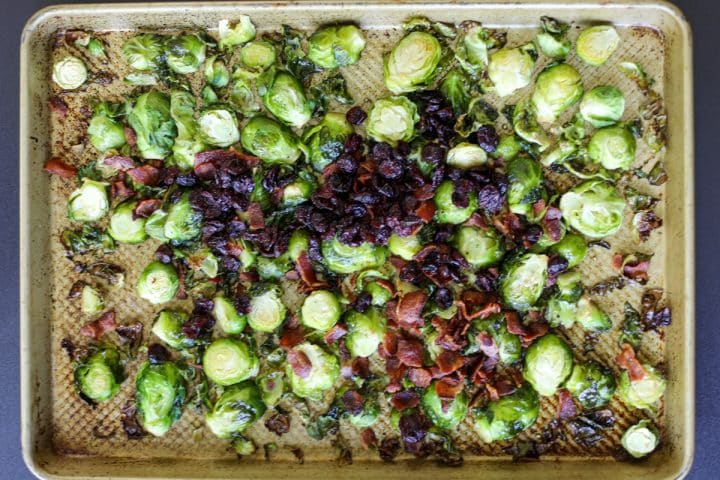 Cooked Brussels sprouts on the tray with cooked and crumbled bacon and dried cranberries.