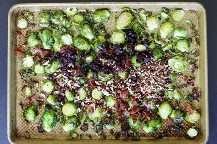 Cooked Brussels sprouts on the tray with cooked and crumbled bacon and dried cranberries and toasted pecans.