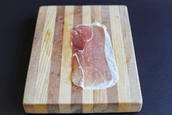 one slice of prosciutto on a cutting board.