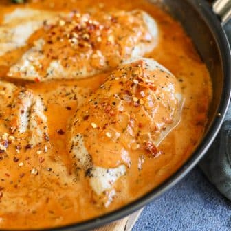 chicken breasts in a pan with pesto sauce.