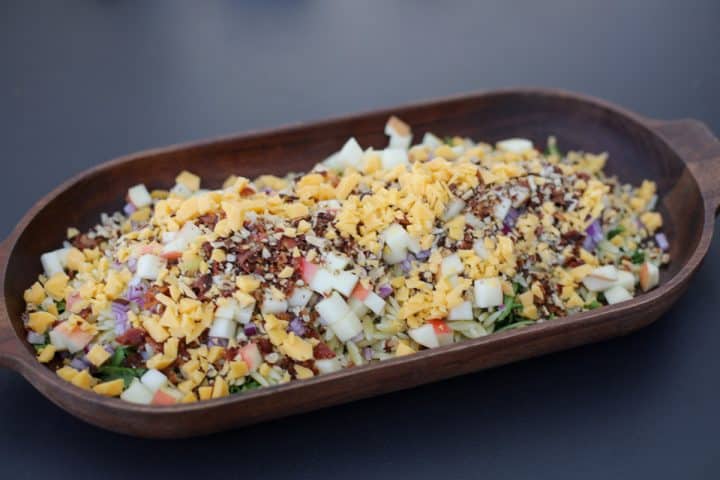 pasta salad being assembled in a serving bowl. 