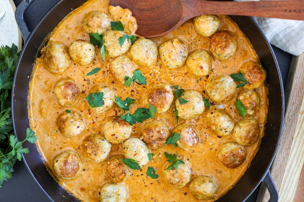 chicken meatballs in a pan with a wooden spoon.