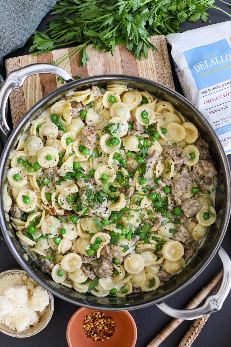creamy pasta with sausage and peas in a pan with Delallo foods packaging. 