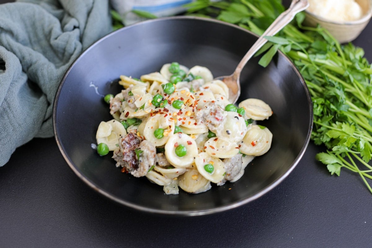 creamy pasta with sausage and peas in a bowl. 