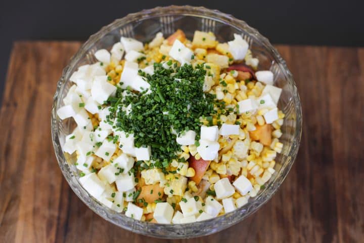 chives peaches, corn, chicken and cheese in a bowl.
