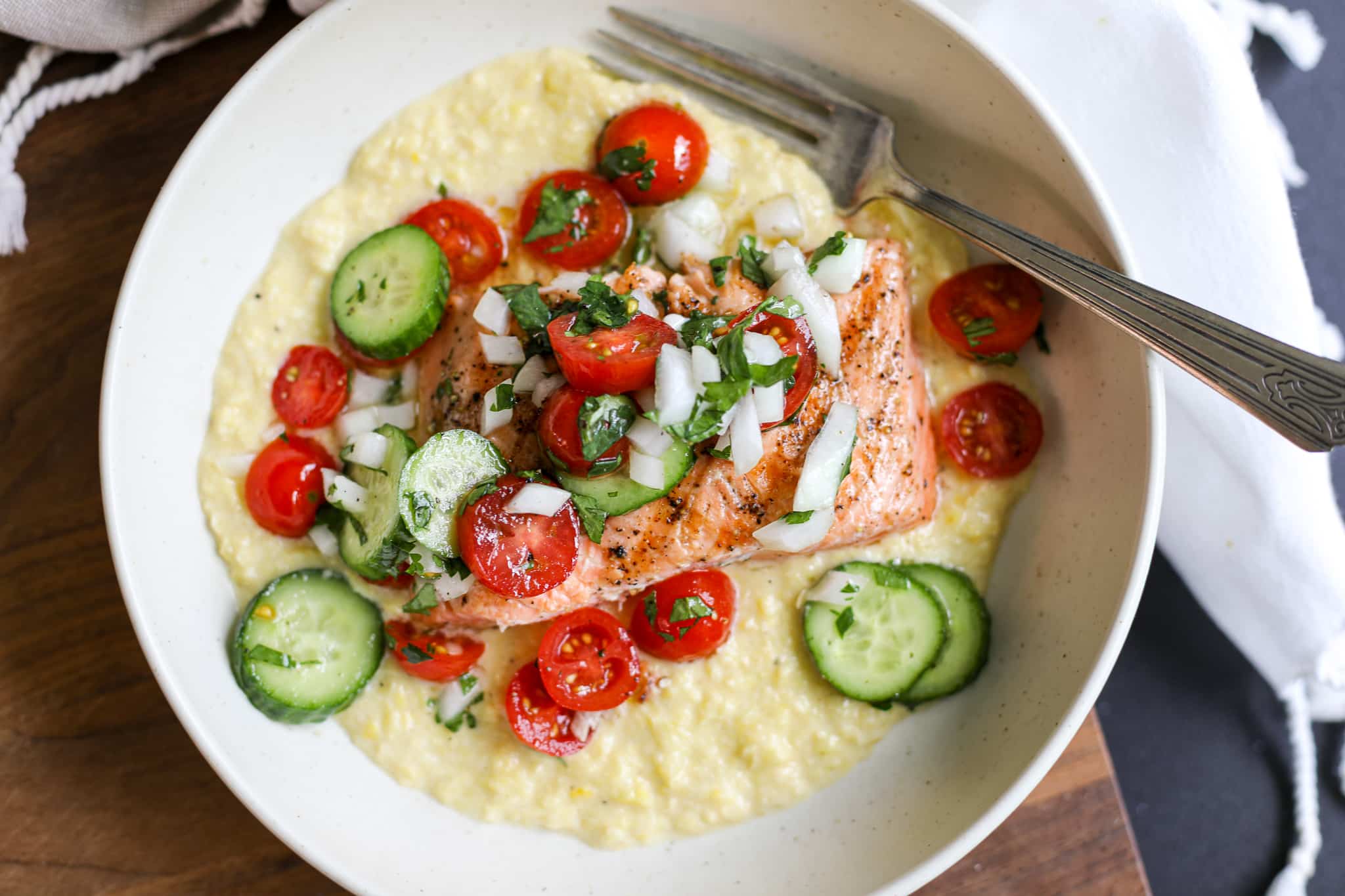 Grilled salmon over creamed corn and tomato salad in a bowl.